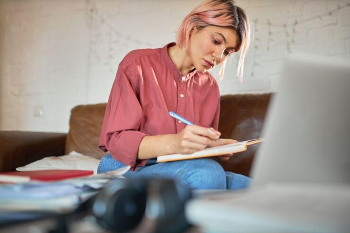 Uma estudante em frente ao seu notebook faz anotações no caderno sobre a Matrícula Online MA 2025