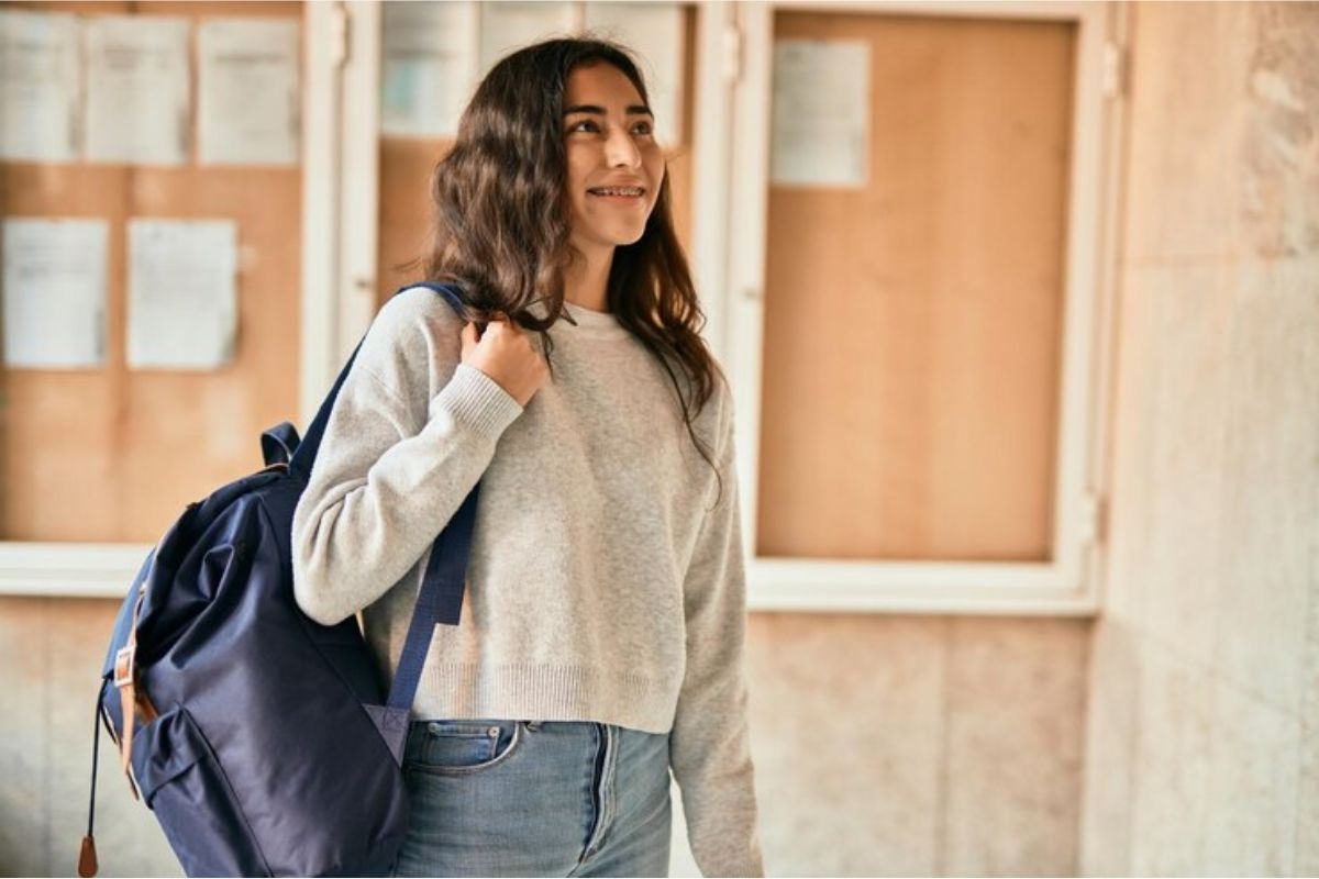 Uma estudante com a mochila nas costas logo na entrada do colégio