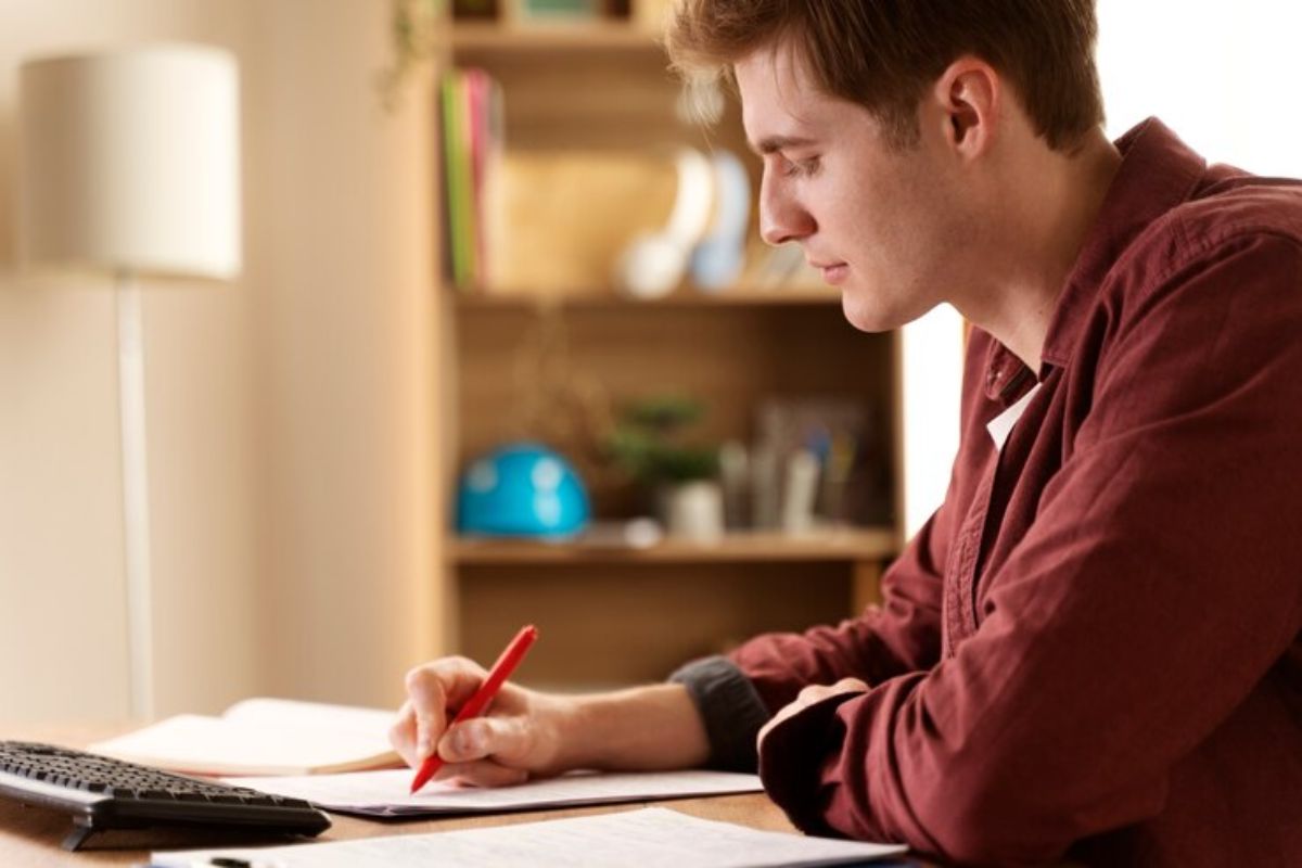 Um estudante anota no caderno as informações que vê em seu notebook sobre a matrícula escolar MT 2025 em seu notebook