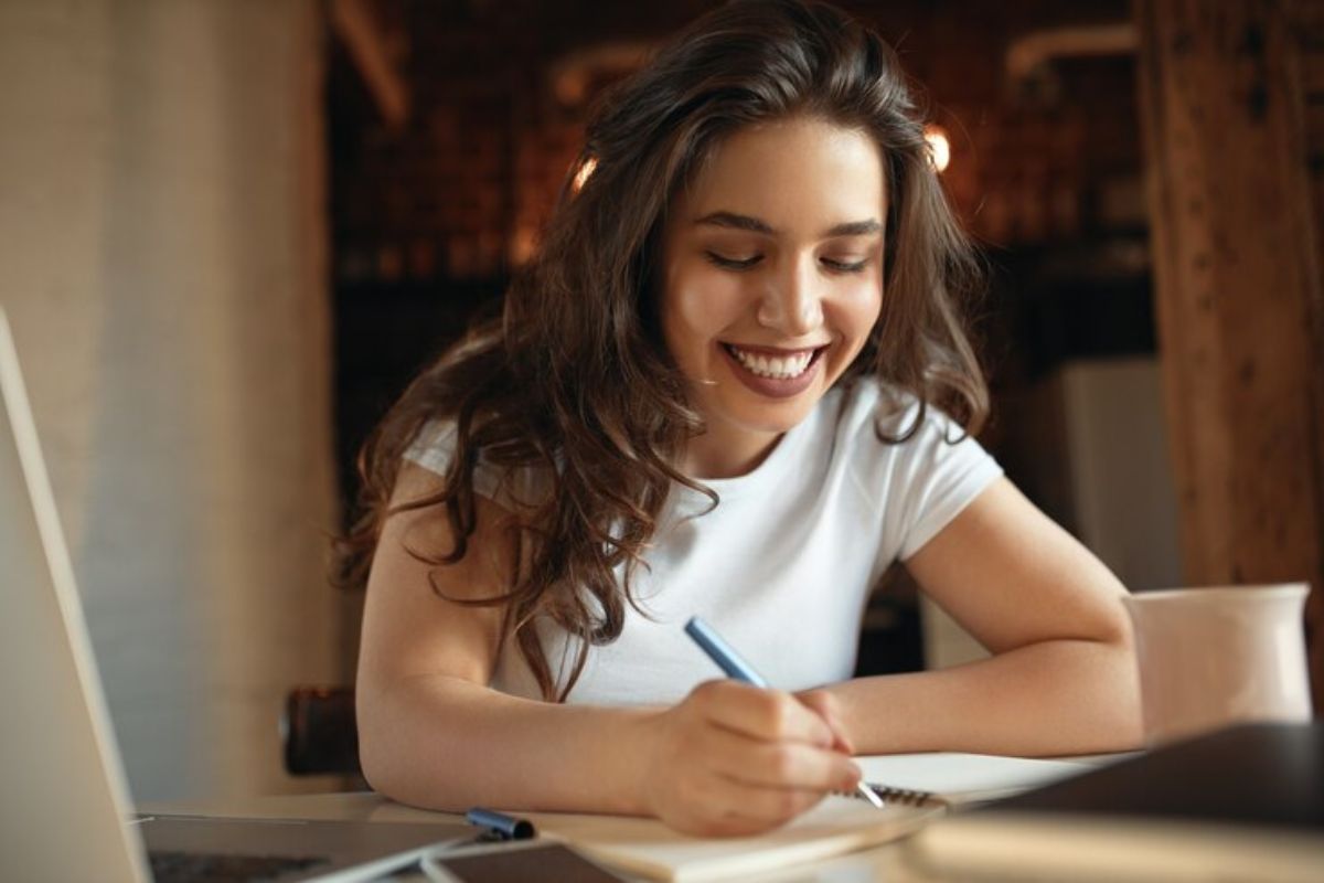 Uma estudante em frente ao seu notebook faz anotações no caderno sobre a Matrícula Online MA 2025