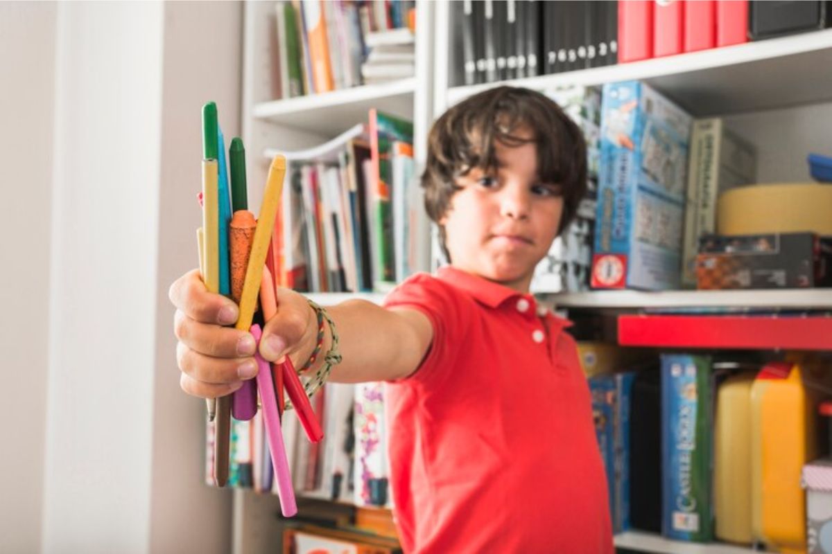 Um menino dentro da escola segurando alguns de seus gizes de cera