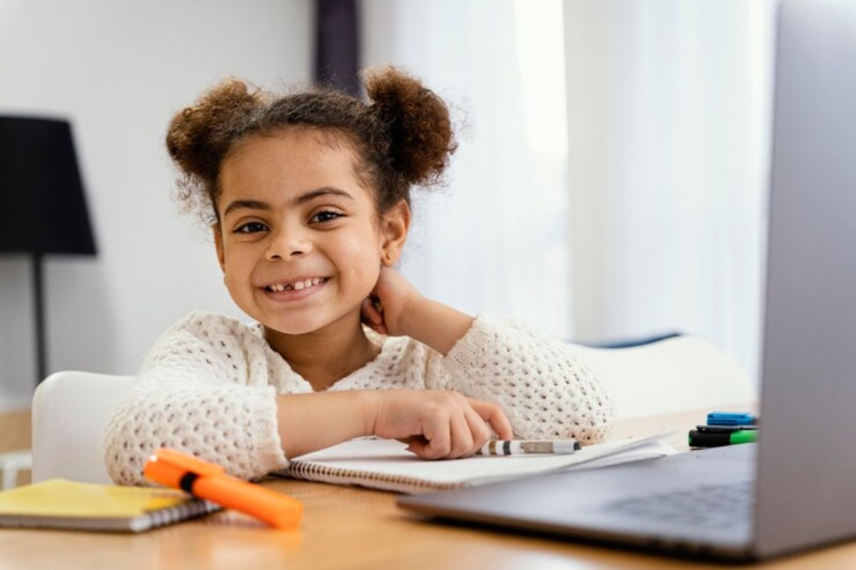 Uma pequena estudante em frente ao notebook parece olhar para a tela onde é feita a sua matrícula escolar Campinas