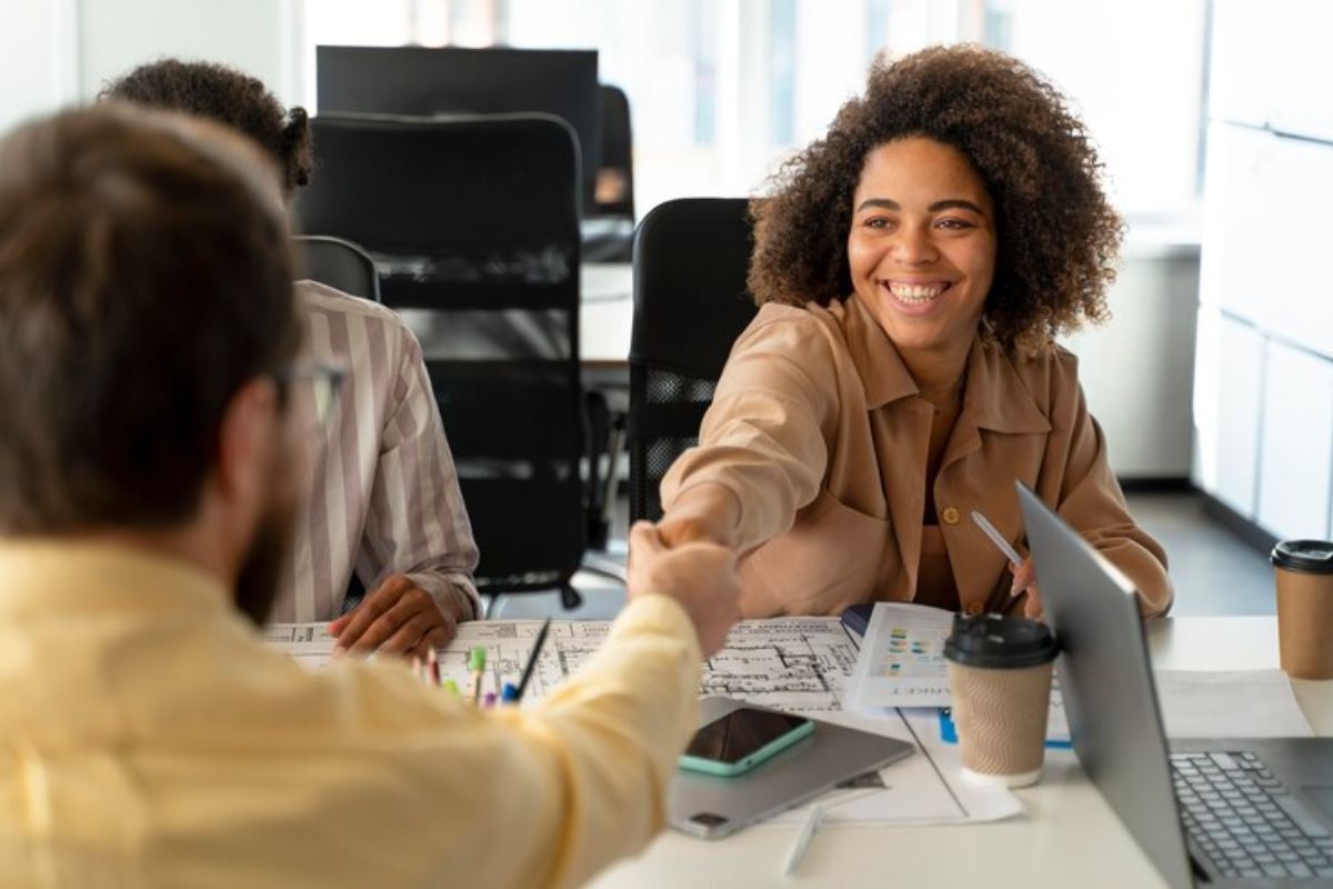 Uma mulher/estudante apertando a mão de um contratante dentro de um escritório