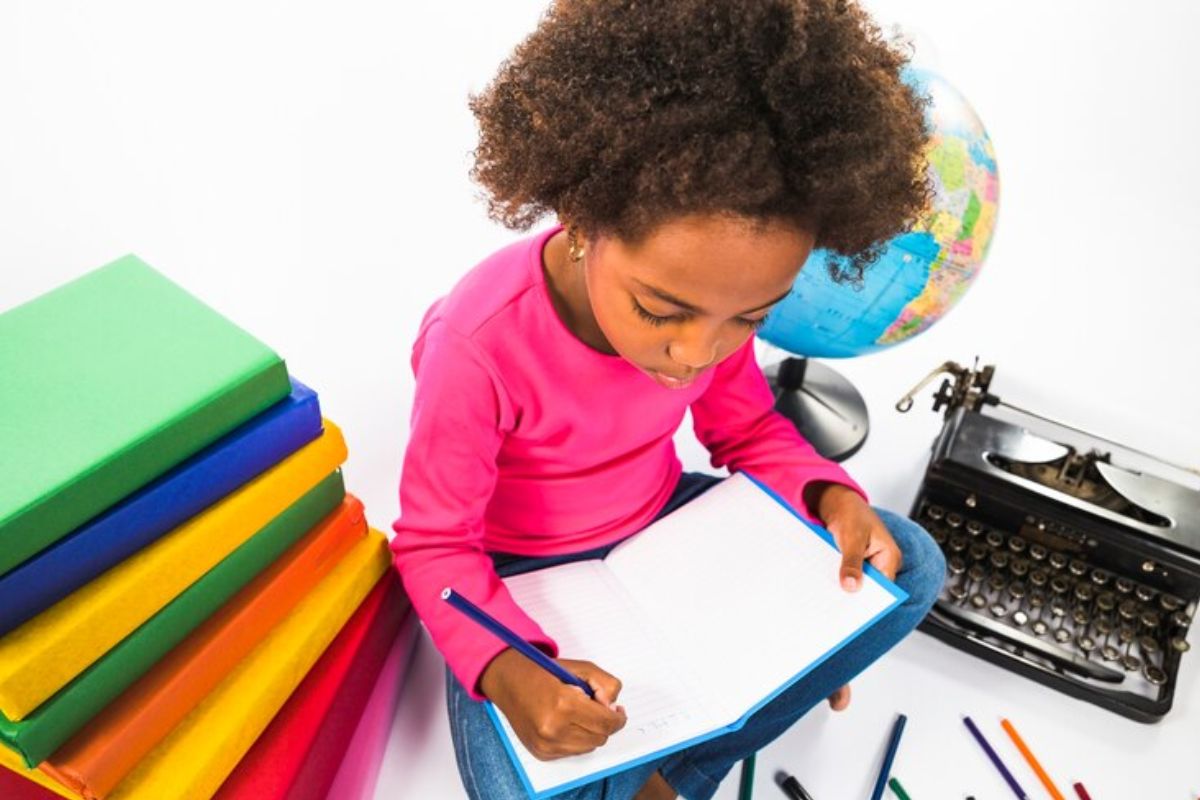 Uma menina escrevendo em seu caderno com diversos materiais escolares após sua mãe ver onde comprar material escolar barato em SP