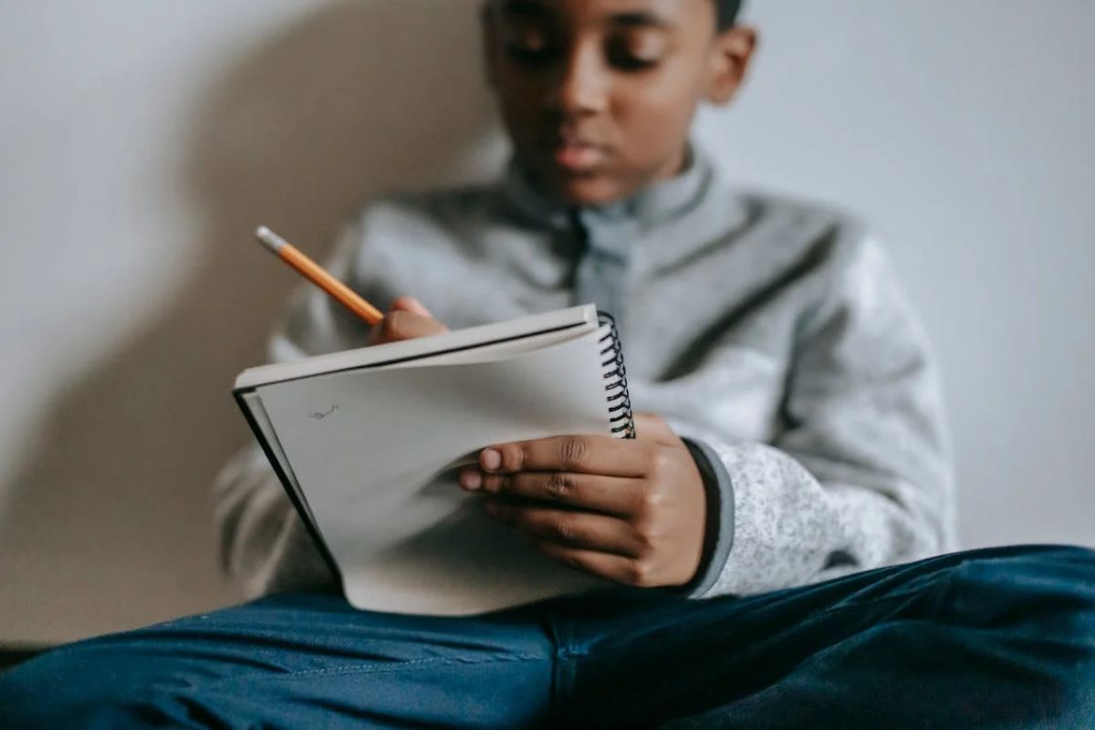 Um estudante com caderno na mão faz anotações com um lápis