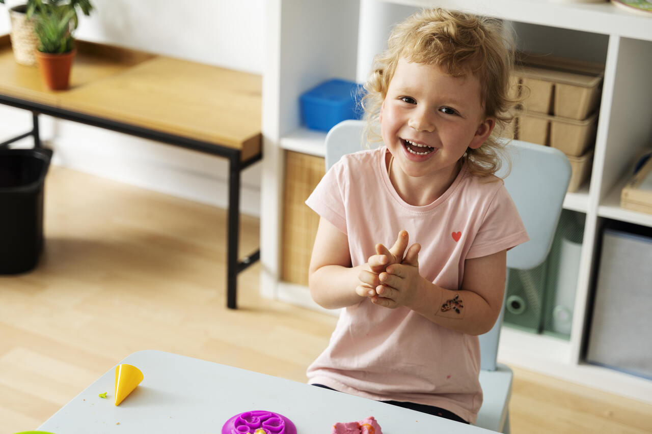 Criança posa sorridente enquanto brinca com massinha na pré-escola 