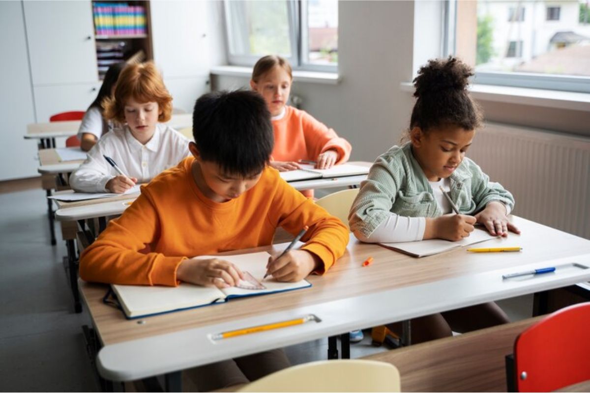 Em uma sala de aula quatro crianças escreve em seu caderno enquanto estudam