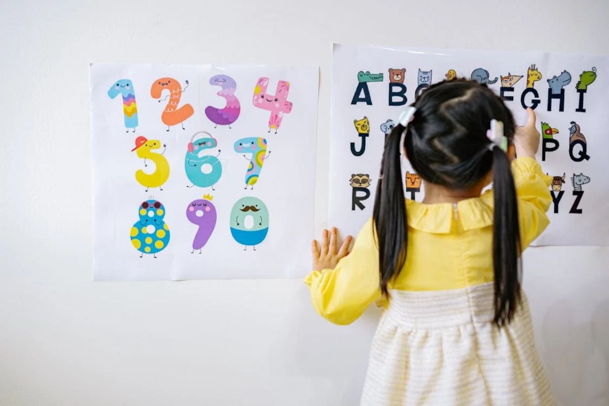 Uma criança em frente a uma parede onde tem as letras do alfabeto e o numeral de 1 - 0