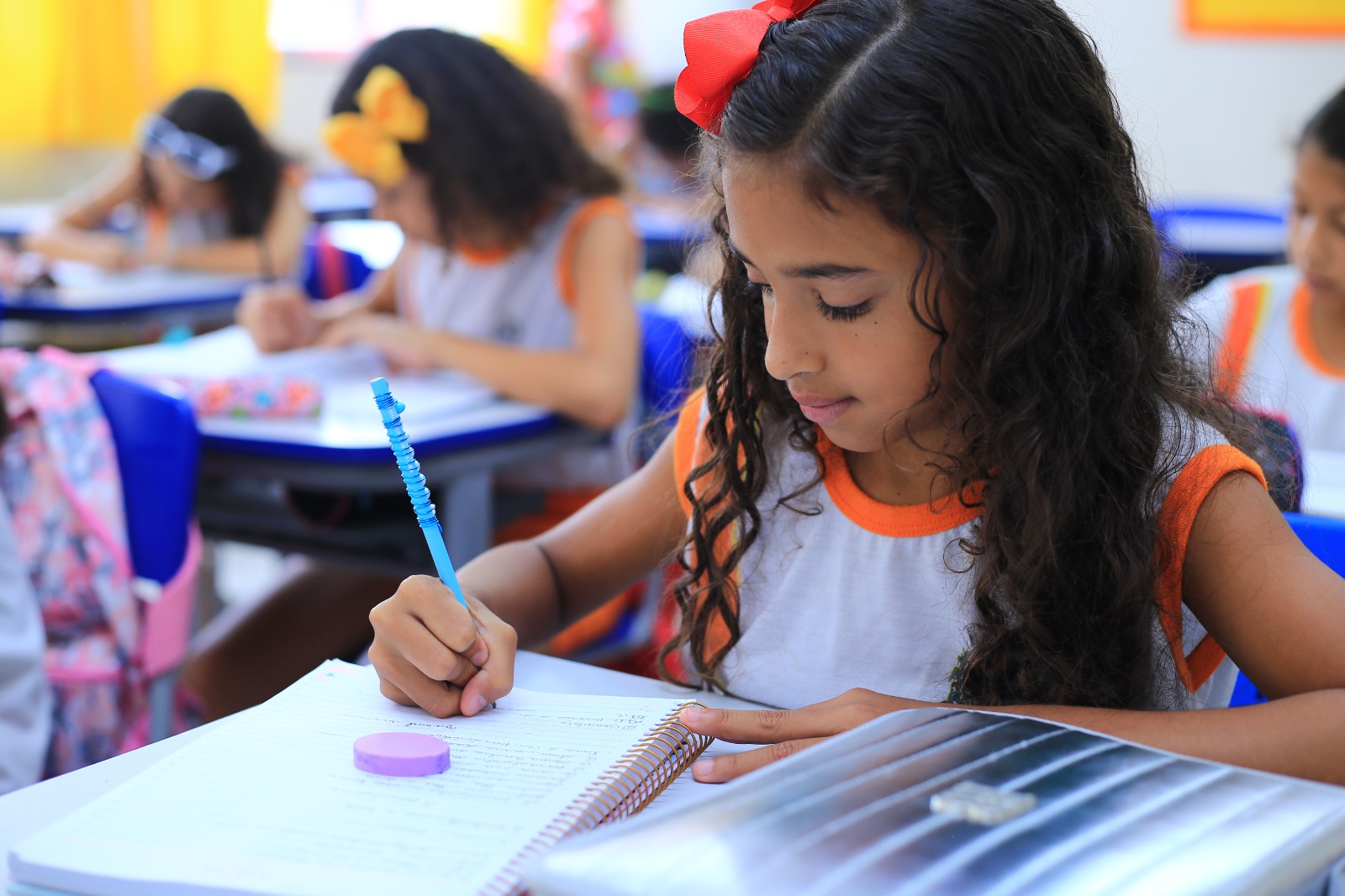 Menina escrevendo em um caderno dentro da sala de aula