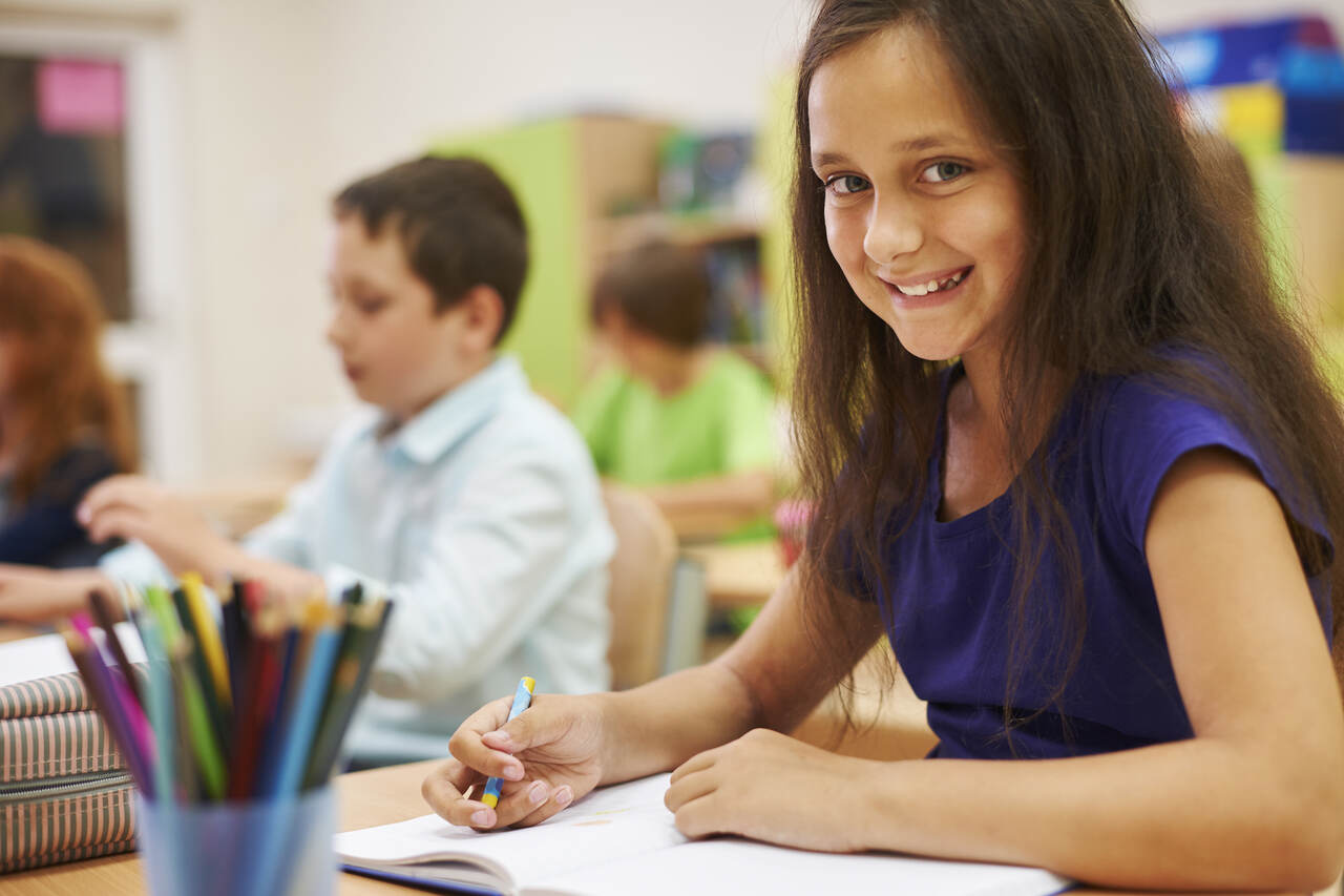 Menina sentada na sala de aula posa sorrindo 