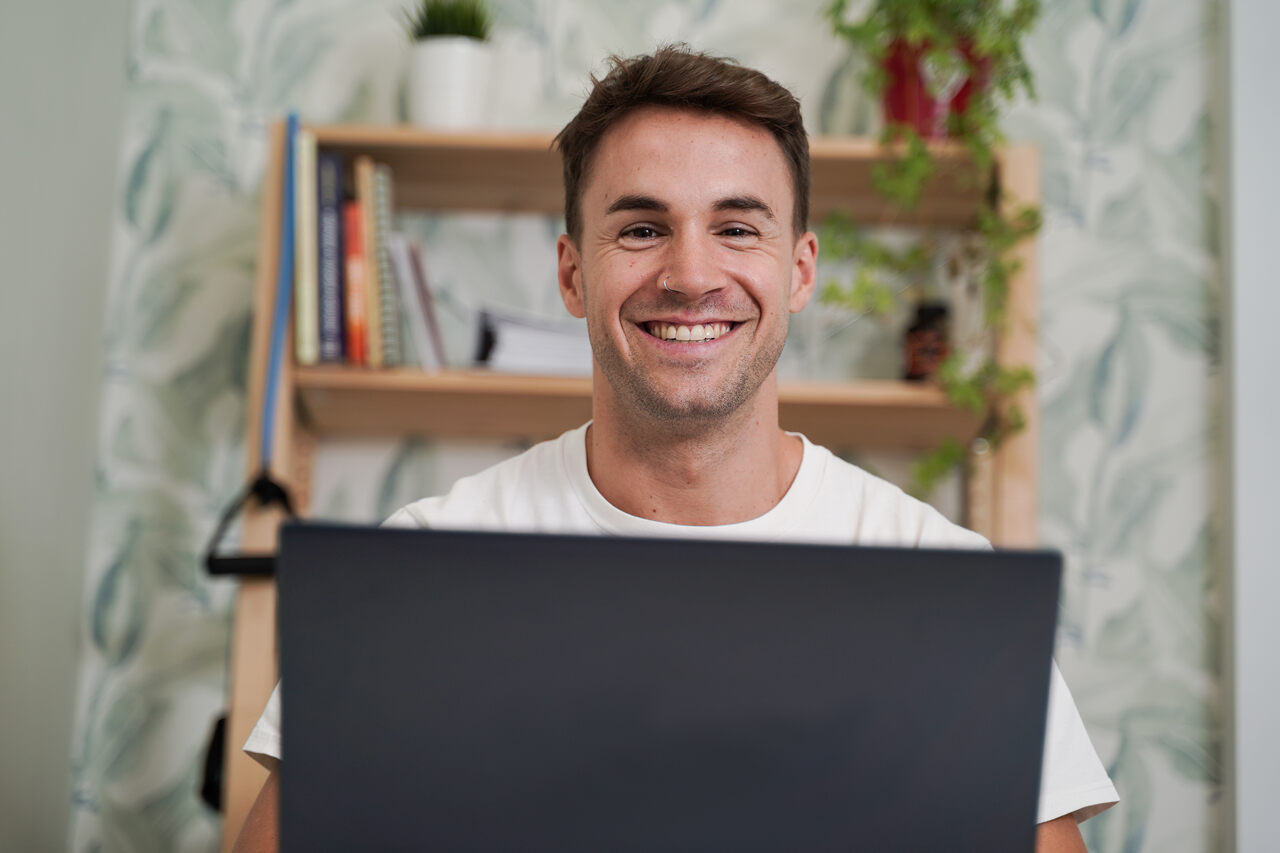 Homem posa sorridente na frente de seu notebook aberto 