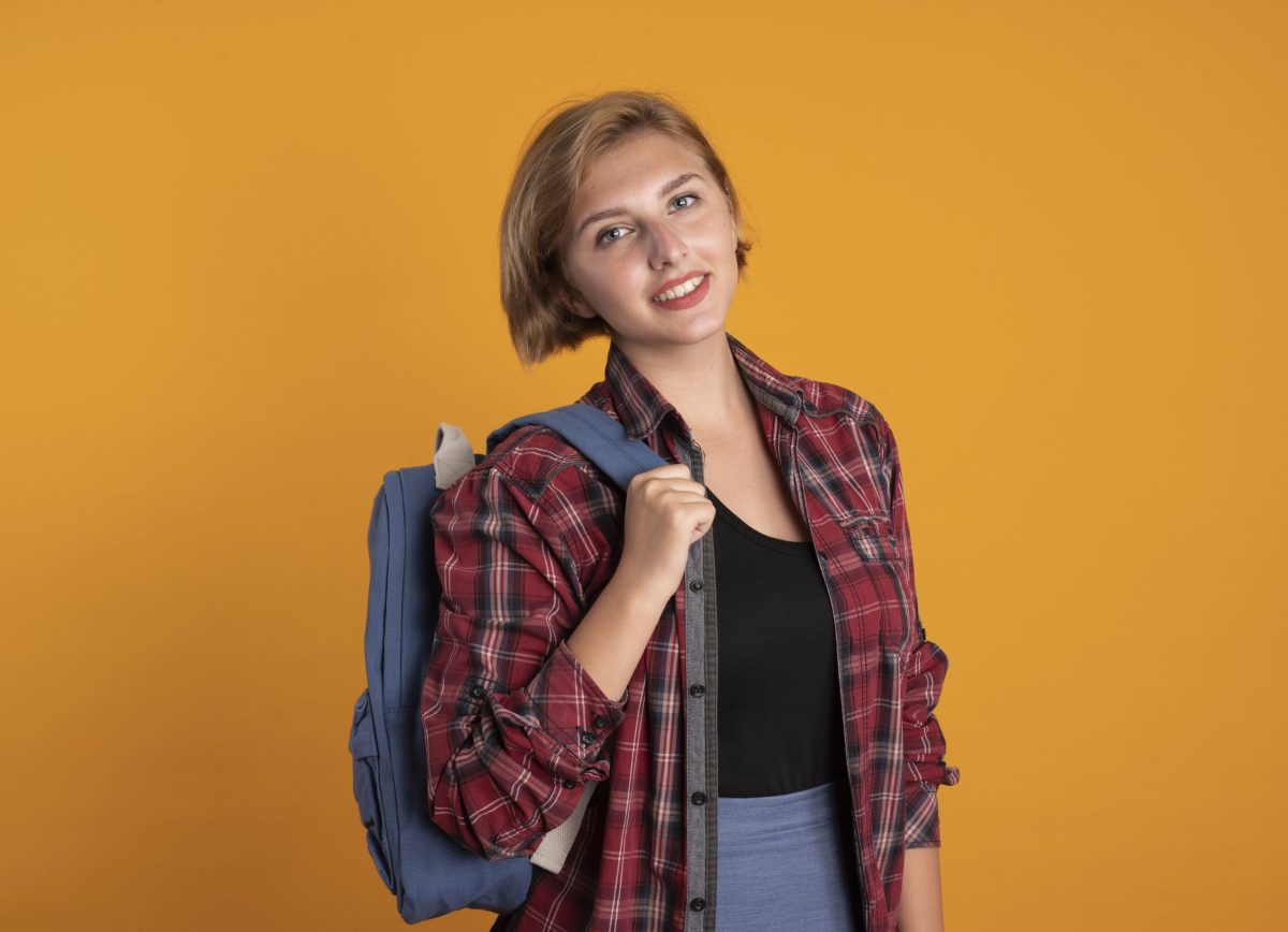 Jovem estudante universitária sorri posa sorrindo carregando uma mochila nas costas 